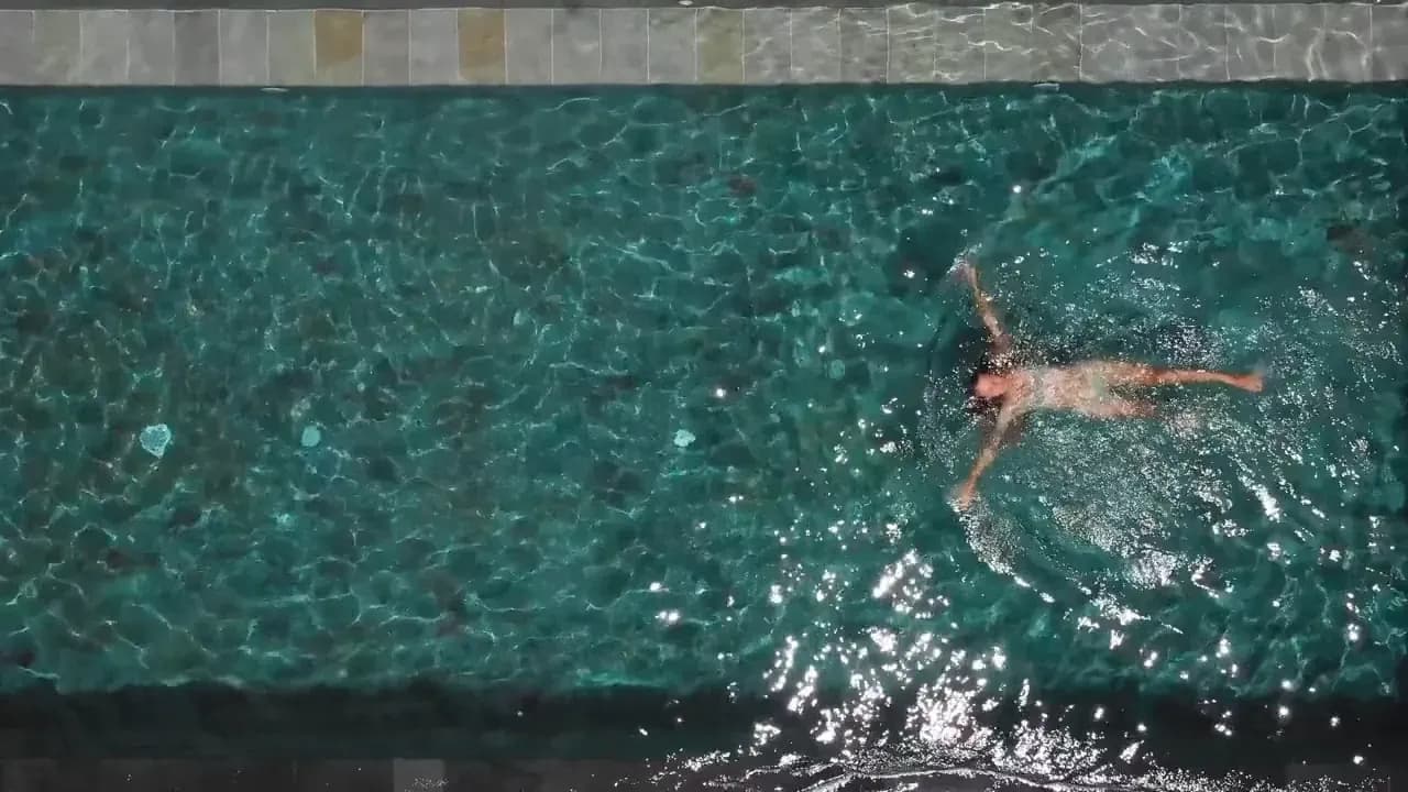 Person swimming in crystal-clear turquoise pool with tiled deck edge visible