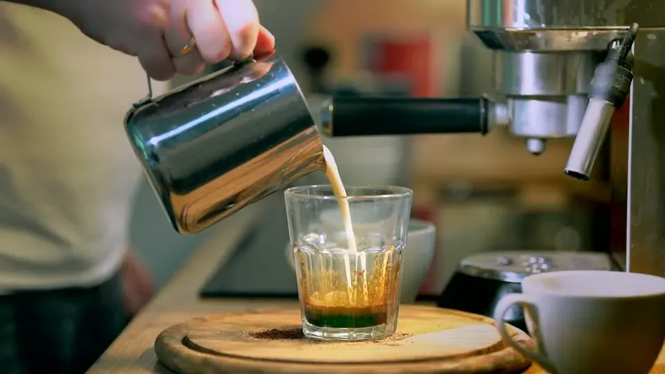 Hand pouring freshly brewed coffee into a glass cup in a modern kitchen